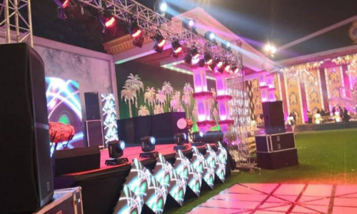 Nighttime event stage with colorful lights, palm-tree backdrop, and LED panels on a decorated venue surface.